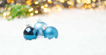Blue Christmas balls laying on the snow on the background of Christmas tree and blurred golden lights with copy space. Preparation for New Year party.の写真素材