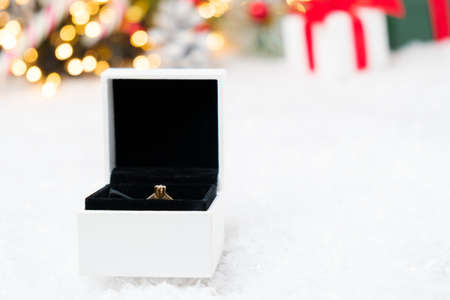 A box with gold ring on the snow with Christmas background. Marriage proposal at New Year Eve