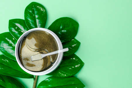 Top view on the plastic jar with golden eye patches and spatula on the green background with leaf and copy space.の写真素材