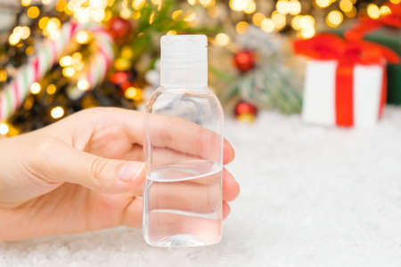 Woman hands holding a sanitizer on the Christmas background. New Year holidays during pandemic of coronavirus.の写真素材