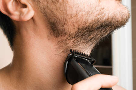 Man shaving beard and neck with an electric razor. Morning routine. Trimming beard with a trimmer.の写真素材