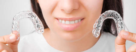 Cheerful young woman holding plastic transparent braces. Orthodontic silicone aligner for whitening...