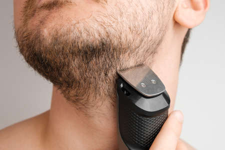 Man shaving beard and neck with an electric razor. Morning routine. Trimming beard with a trimmer.の写真素材