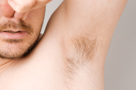 Close up of man armpit with long unshaved hair and pinching nose from sweaty bad smellの写真素材