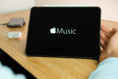 Apple music logo on the screen of iPad tablet with smart phone iPhone charging on the wireless...