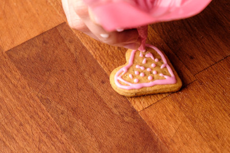Icing of Valentines Day. Woman decorating gingerbread cookies in the shape of heart on a wooden table.の写真素材