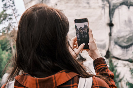Close up woman in a red shirt making a photo or a video of the rock and forest using her smartphone. Turisme concept. Hiking in the mountainsの写真素材