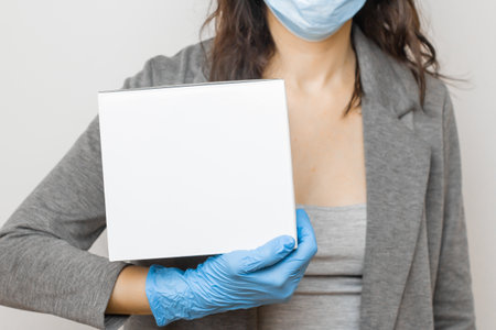 Woman holds a white donation box in protective mask and rubber gloves. Concept of charity volunteer during pandemic of virus.の写真素材