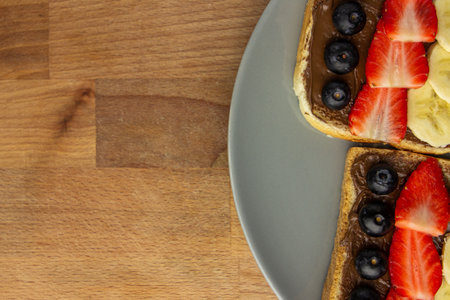 Toast bread with blueberry, strawberry and banana on a grey plate on a wooden background for copy...
