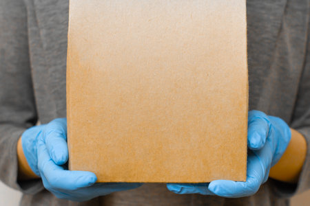 Delivery from online shops during quarantine. Woman holds a cardboard box with copy space in rubber...