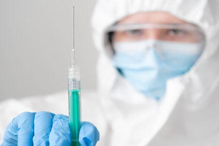 Vaccine in the syringe for prevention of virus in doctor hand, wearing protective mask and protective PPE suit and rubber gloves.の写真素材