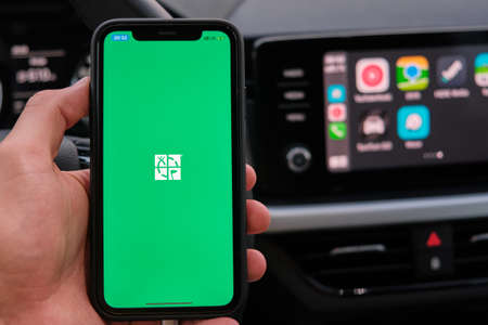 XXX on the screen of smart phone in mans hand on the background of car dashboard screen with application of navigation or maps. January 2021, Prague, Czech Republic.のeditorial素材