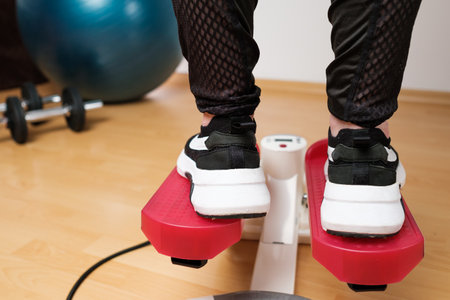 Back view on the woman feet in sneakers doing exercising on the twist stepper or stair stepper...