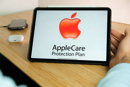 Apple Care logo on the screen of iPad tablet with smart phone iPhone charging on the wireless charger and airpods in the case on the background, November 2020, San Francisco, USAのeditorial素材