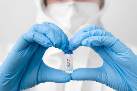 Covid-19 vaccine in doctors or nurses hands in the form of heart in blue rubber gloves. Prevention...