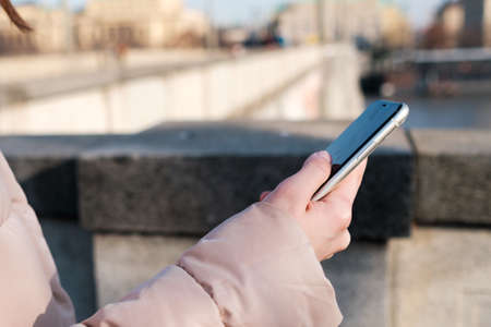 Close up woman hands holding a smartphone. Young girl uses messenger, free wi fi or internet connection outside in the street.の写真素材