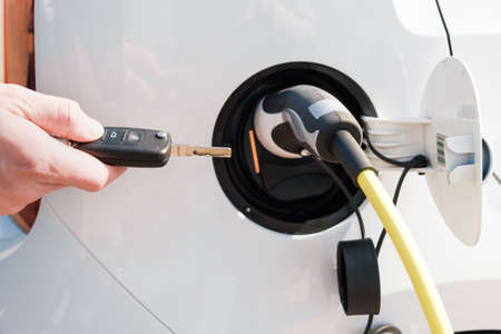 Charging an electric vehicle with a power cable supply plugged in and mans hand unblocking it with a...