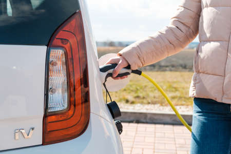 Close up woman plugging a power supply into an electric car at charging station in the street, March 2021, Prague, Czech Republic.のeditorial素材