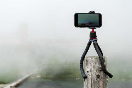 Smartphone on the tripod taking photos. Capturing image or time lapse of moving clouds in the mountains. Device for bloggingの写真素材