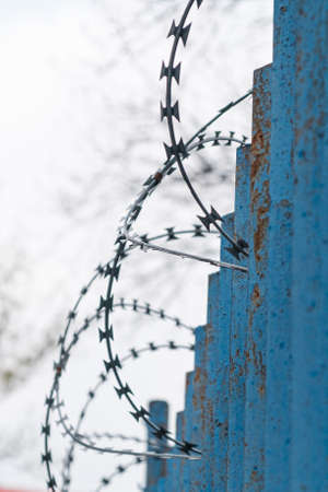 A blue fence with barbed wire near prison or mental hospital on the background of grey sky.の写真素材