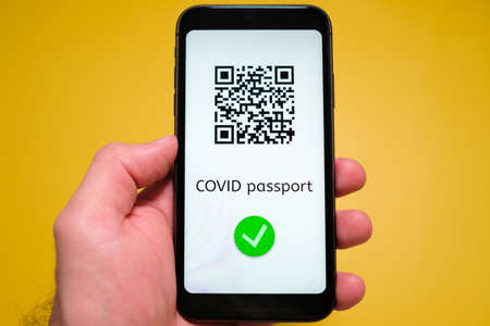 Covid pass with QR code on the screen in smartphone in mans hand on the yellow background, May 2021, San Francisco, USA.の写真素材