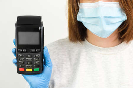 Woman in rubber gloves and face mask holding a POS terminal for payment during pandemicの写真素材