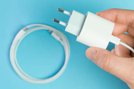 A white smart phone charger cable with lightning hi speed USB type C connector and adapter in man hand on the blue background.の写真素材