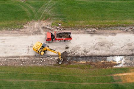 Excavator digging ground near the field and loading to the truckの写真素材