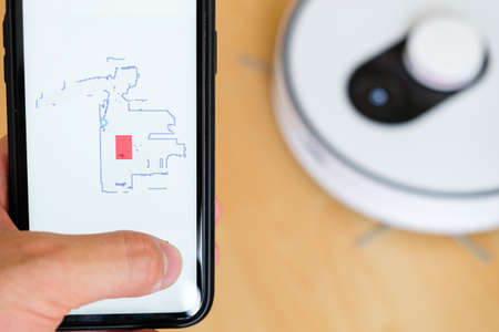 Close up a mobile phone application for managing of robot vacuum cleaner in mans hand. Smart...