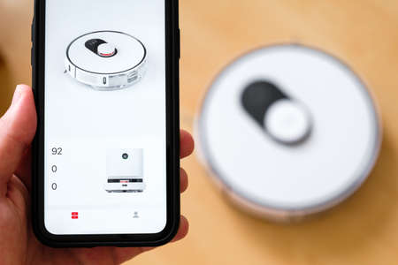 Close up a mobile phone application for managing of robot vacuum cleaner in mans hand. Smart technology for housekeepingの写真素材
