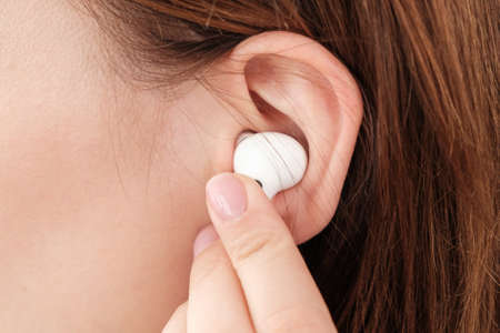 Woman inserts wireless headphone in the ear.
