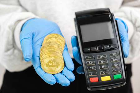 Bitcoin coins and pos terminal in woman hands in rubber gloves.の写真素材
