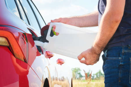 Close up woman refilling the red car with fuel or a diesel engine fluid from canister in the field.の写真素材