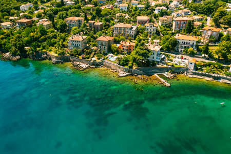 Beautiful villas near the coast of rocky beach in a small town Lovran, Croatia. Arial view of Lungomare sea walkway with transparent water.の写真素材