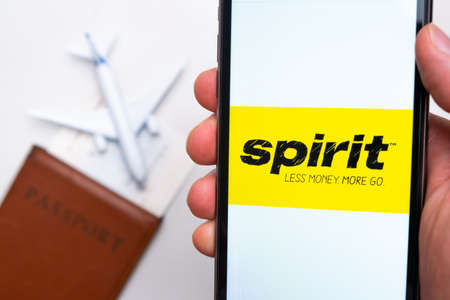 Spirit airlines logo on the screen of smartphone on the background of passport, ticket and plane,...