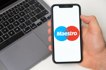 MaestroXxx financial platform for money transfer using smartphone. Man hand holding a mobile phone with application on the screen and notebook on the background. November 2021, San Francisco, USAのeditorial素材