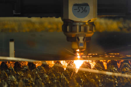 Contemporary laser cutter carves thin metal sheet with bright sparks in dark workshop of modern production plant extreme closeupの写真素材