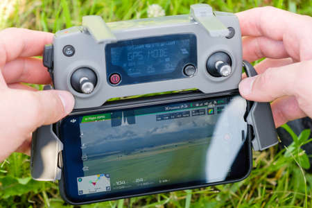 Close up the drone console controller with the mobile phone in mans hands with grass on the...