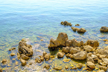 Rocky coastline with big stones in transparent blue water of sea in sunny day.の写真素材