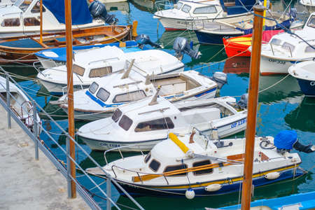 Small fishing motorboats moored to wooden poles on shore reflecting on dark sea water at local port of coastal city on sunny summer dayの写真素材