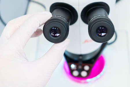Close up scientist hand sets up a microscope to analyze the sample.