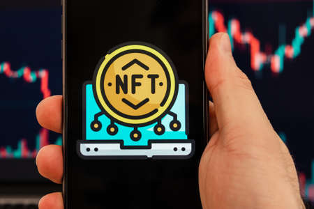 NFT logo on the smartphone screen in a mans hand, stock price chart in the background. Stocks rise and fall. February 2022, San Francisco, USA.のeditorial素材