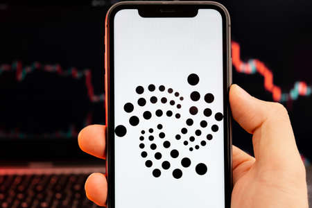 IOTA MIOTA app of cryptocurrency stock market analysis on the screen of mobile phone in man hands and downtrend charts trading data on the background, February 2022, San Francisco, USA.のeditorial素材