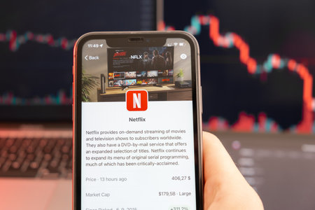 Netflix stock price downtrend with red graphs on the background. Man hands holding a smartphone with on the screen, February 2022, San Francisco, USA.のeditorial素材