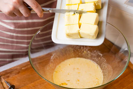 The dough preparation process. Female hands add butter into the mixing bowl for baking cake on a...