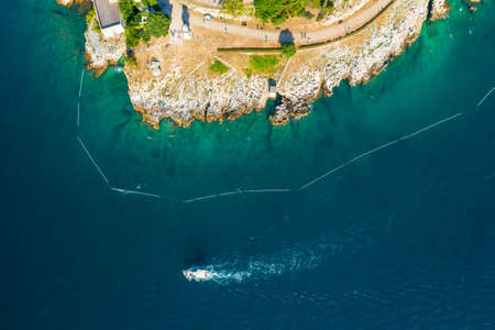 Yacht sails in Adriatic sea and leaves white seafoam trail near Rovinj rocky beach. Azure bay surrounding Croatian town at bright sunlight. Aerial viewの写真素材