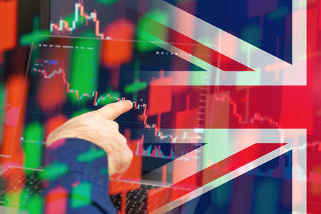 UK downtrend of the economy in a world crisis. Man hand shows on the decreasing candle stick graph chart in the stock market with the flag on the background, March 2022, San Francisco, USAの写真素材