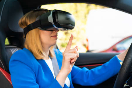 Businesswoman in the VR googles sitting in the car and turning the steering wheel in a car. Having and fun and playing games with augmented realityの写真素材