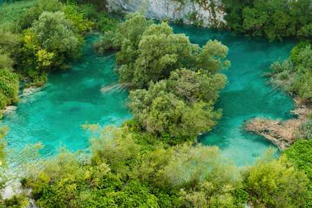 Small green islands among turquoise-colored transparent water of lake surrounded by mountains. Breathtaking landscape of natural reserve on Plitvice lakes upper viewの写真素材