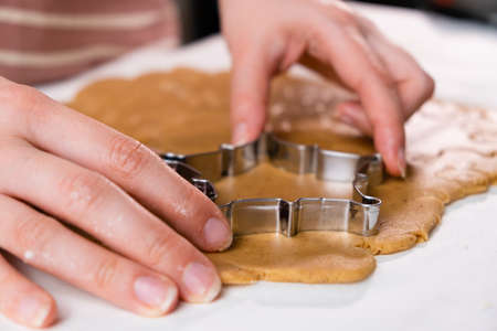 Close up woman hands cutting out cookies with metal mold from the shortcrust pastry. A metal forms in the form of snowflakes for making gingerbread for Christmas.の写真素材